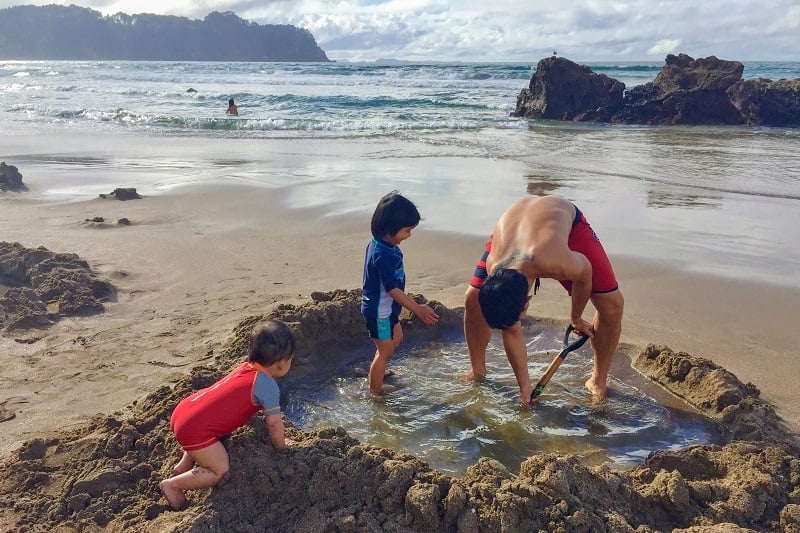 Family digging a pool at Hot Water Beach during their motorhome holiday