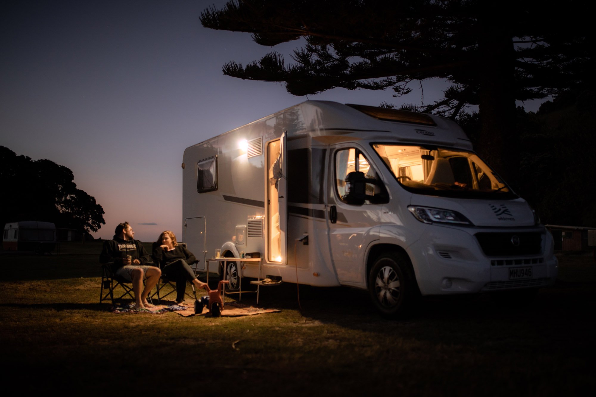 mum and dad outside motorhome on camping chairs while baby naps