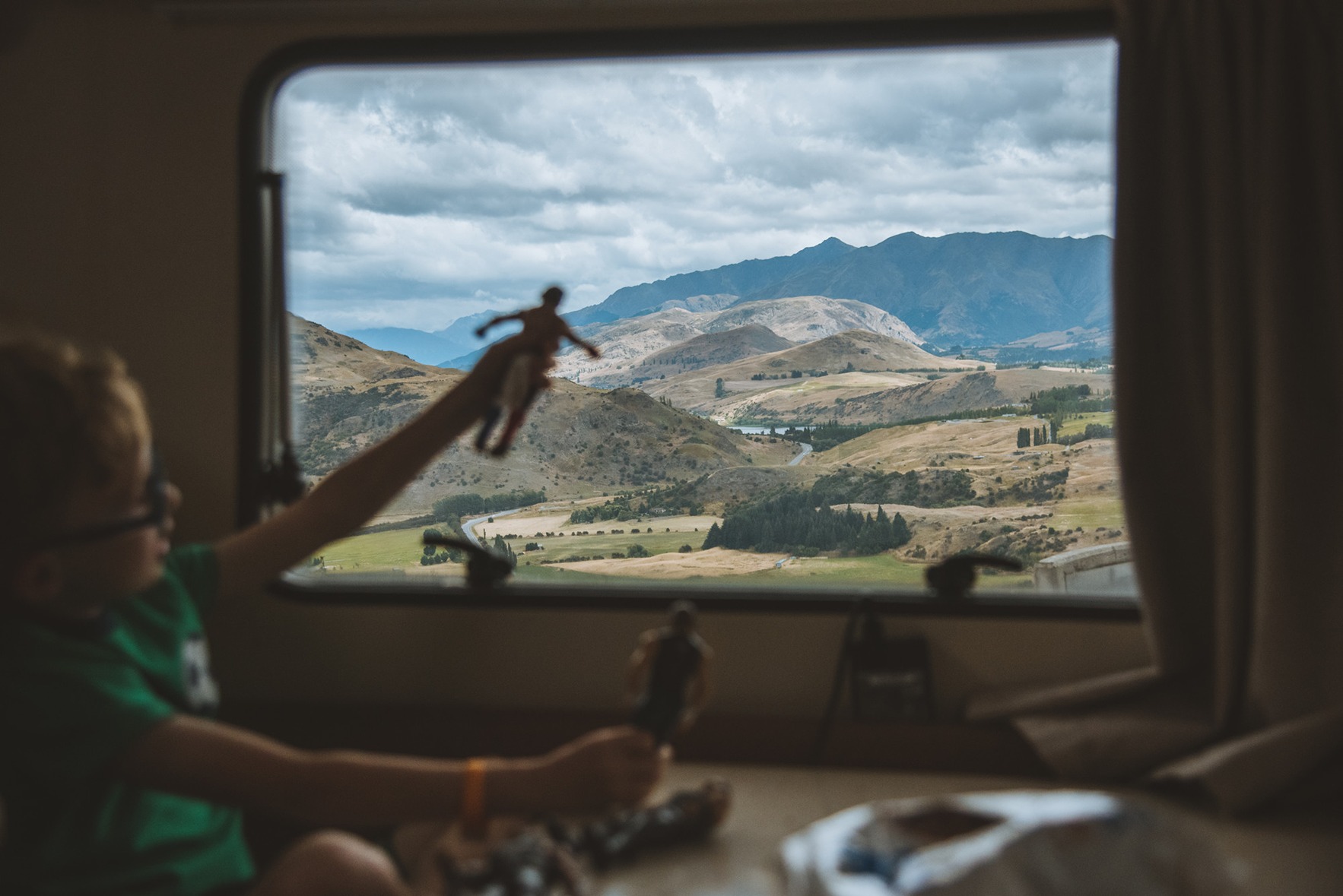 Child playing a toy beside a motorhome window with hills in the backdrop