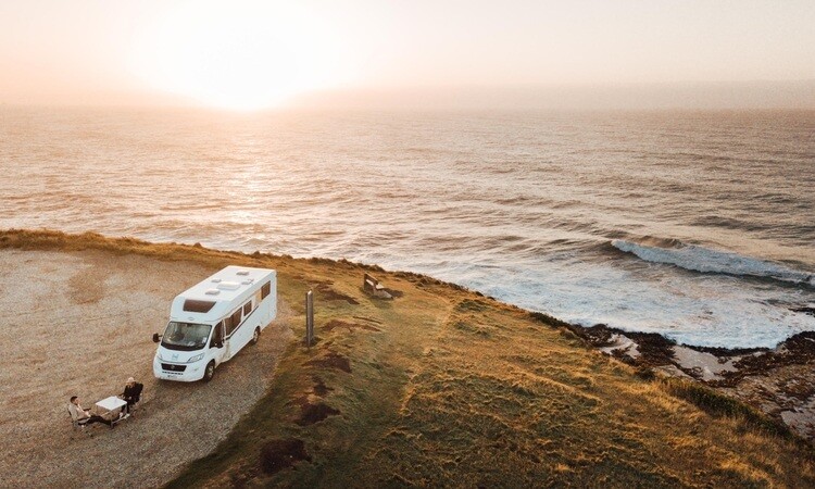 A couple wild camping with a Wilderness Motorhome beside with a coastal view in New Zealand