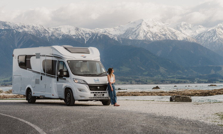 A woman leaning beside her Wilderness motorhome enjoying a snow-capped mountain view