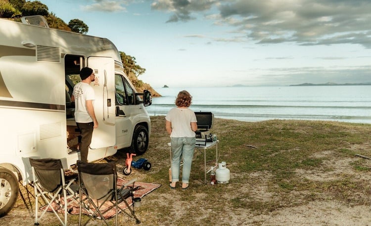 Couple cooking on BBQ on the beach with motorhome