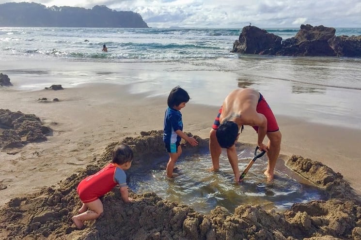 Family digging a pool at Hot Water Beach during their motorhome holiday