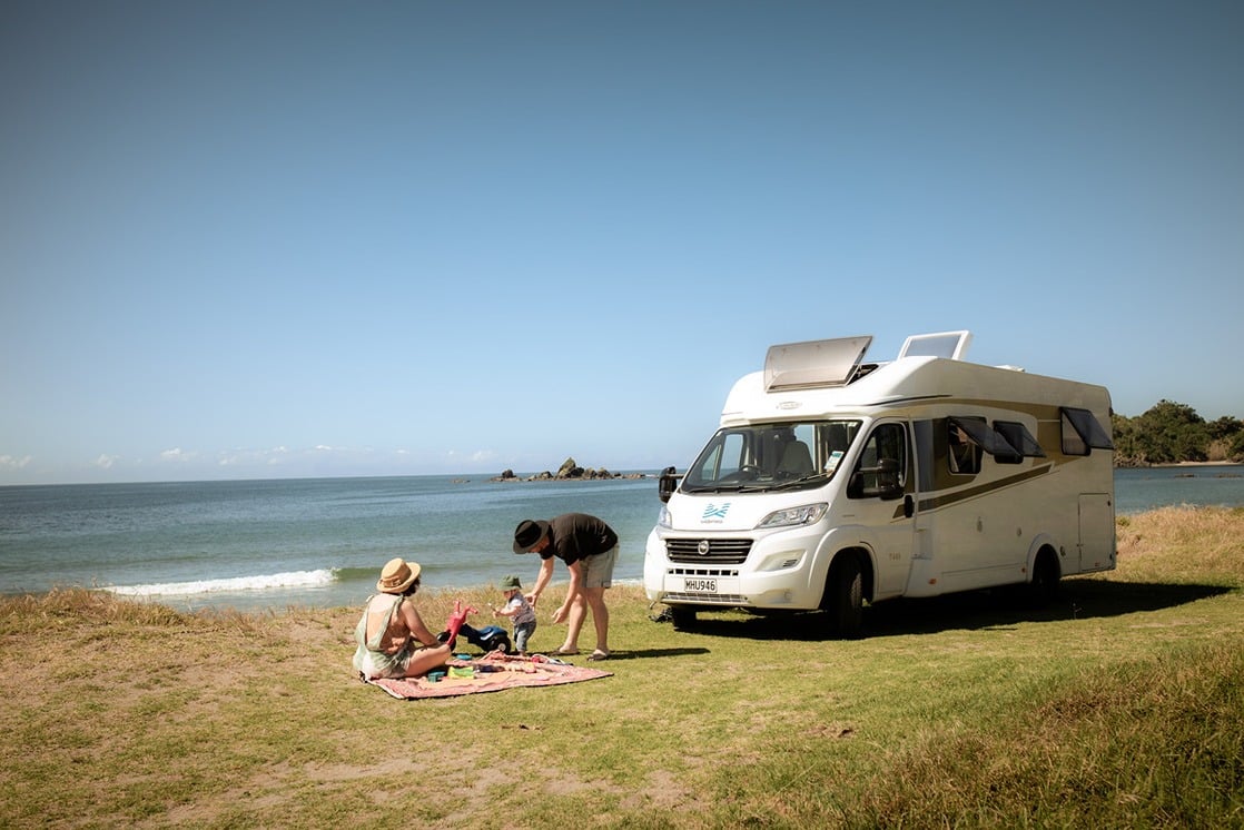 Family picnicking outside of motorhome beside a beach